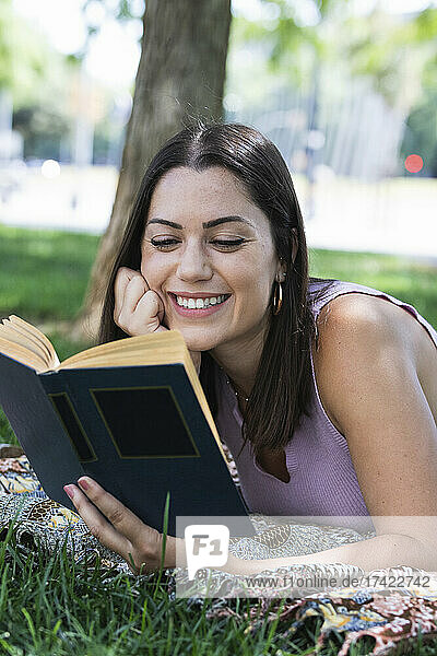 Smiling woman reading book while lying on blanket in park