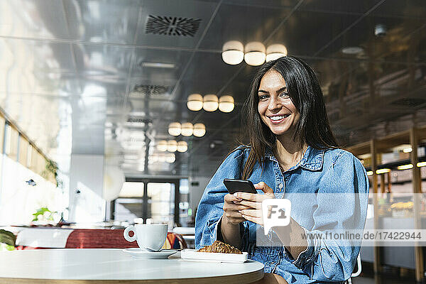 Schöne Geschäftsfrau mit Mobiltelefon sitzt im Café