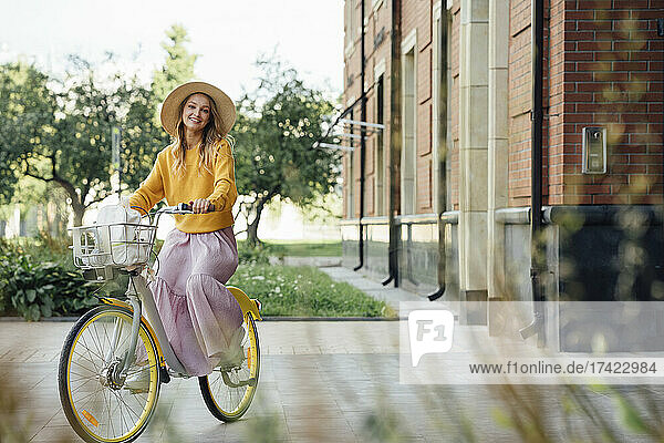 Woman wearing hat riding bicycle by building