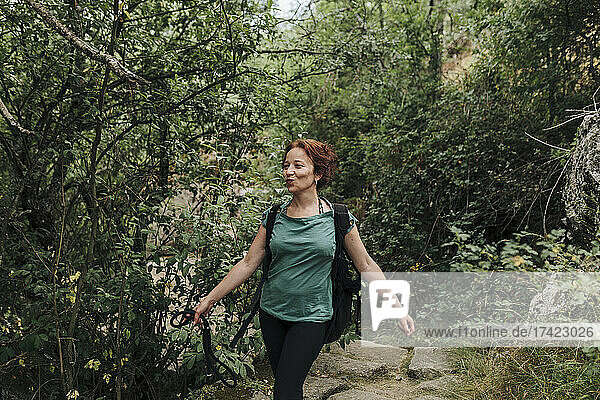 Lächelnde Frau mit Haustierleine  die im Wald spaziert