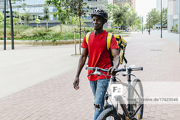 Smiling delivery man with bicycle walking on footpath