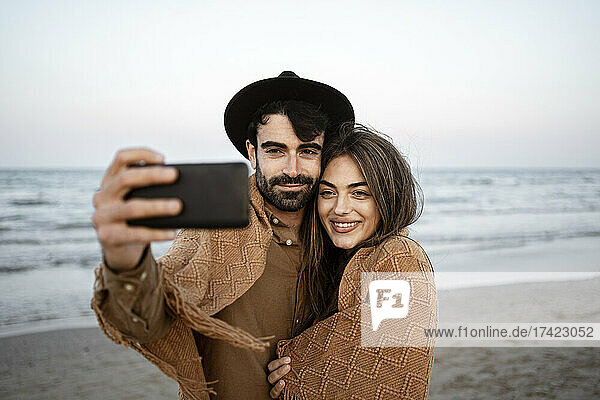 Boyfriend taking selfie with girlfriend through mobile phone at beach