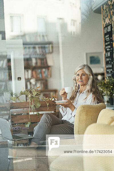 Businesswoman holding coffee cup while sitting on chair in cafe
