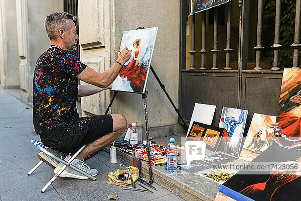 Männlicher Maler malt auf Leinwand  während er auf der Straße sitzt