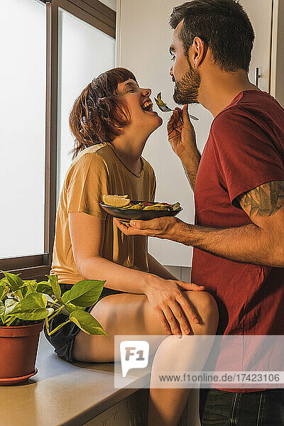 Man feeding girlfriend with salad in kitchen at home