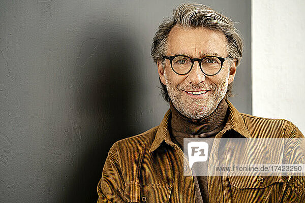 Smiling mature man with hair stubble by wall