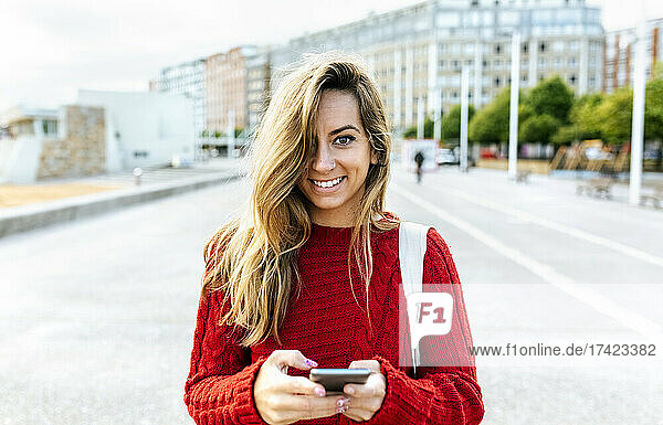 Smiling woman holding smart phone while standing on road