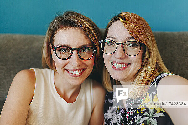 Cheerful female freelancers in eyeglasses sitting on sofa at home