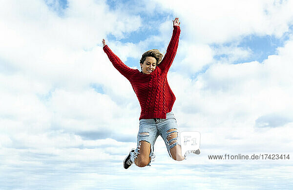 Carefree woman with arms raised jumping in front of sky
