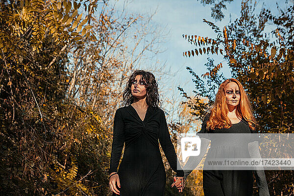 Friends with spooky make-up holding hands while walking in forest