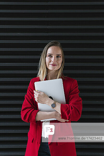 Smiling businesswoman with laptop in front of black shutter