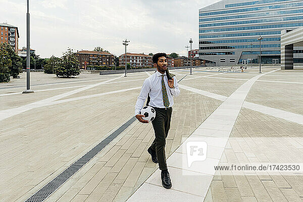 Businessman with soccer ball and blazer walking on footpath