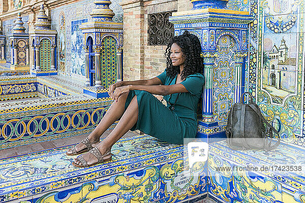 Smiling young woman with curly hair sitting at Plaza De Espana  Seville  Spain