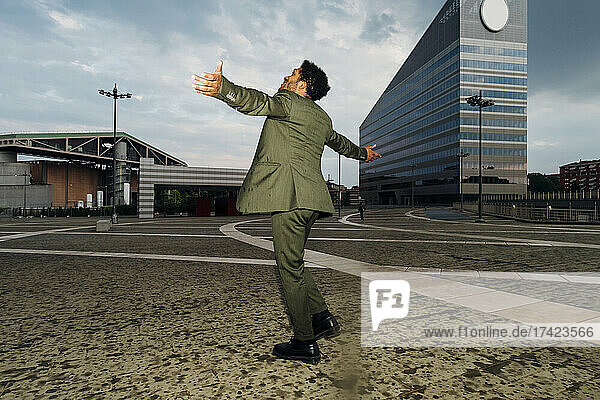 Businessman with arms outstretched spinning on footpath
