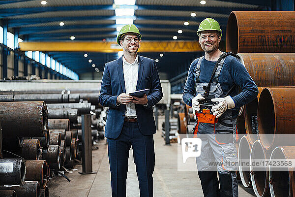 Smiling male manager standing with warehouse worker in factory