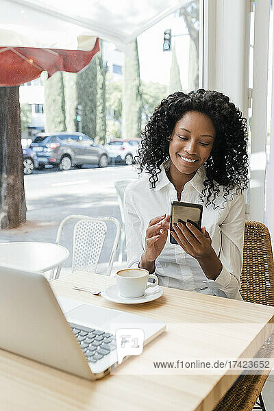 Smiling female freelancer using mobile phone while sitting at cafe