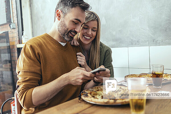 Bearded man sharing mobile phone with female friend at table