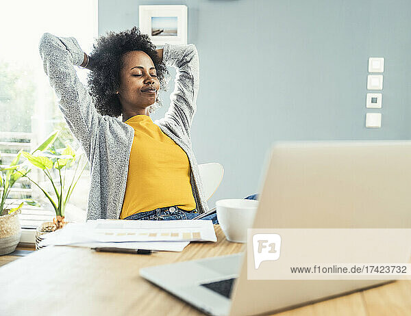 Young businesswoman with hands behind head relaxing at home office
