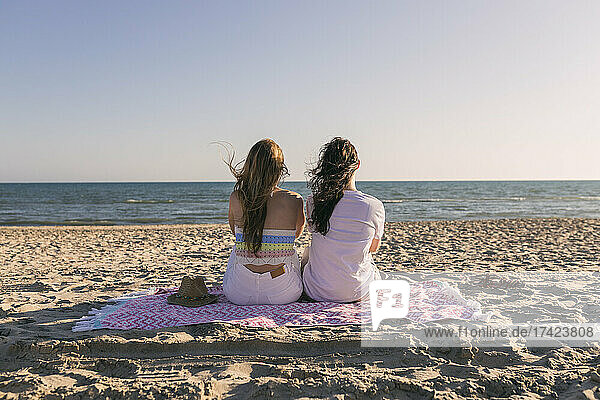 Freundinnen schauen auf das Meer  während sie auf einer Picknickdecke sitzen