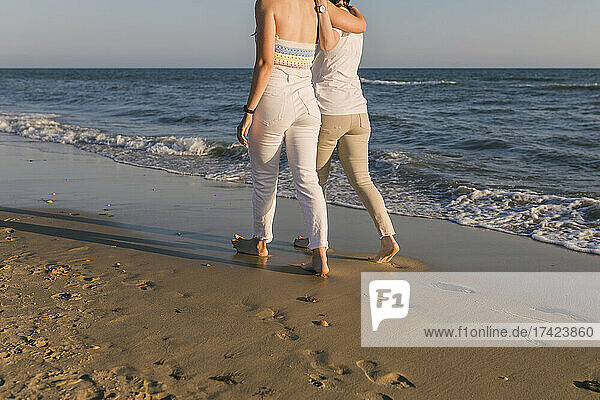 Female friends walking together on shore at beach