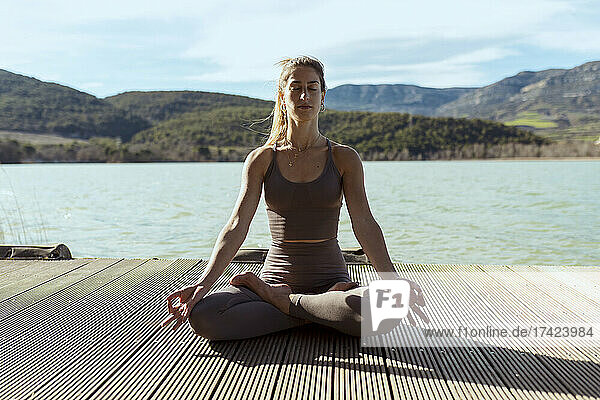 Frau mit geschlossenen Augen meditiert  während sie an einem sonnigen Tag im Lotussitz sitzt