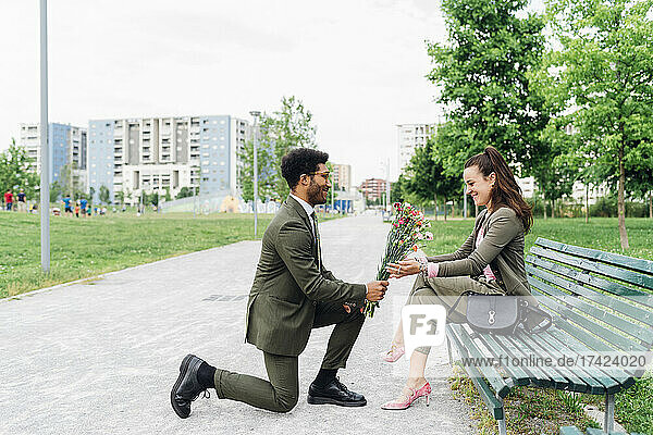 Businessman giving bouquet to colleague while kneeling on footpath