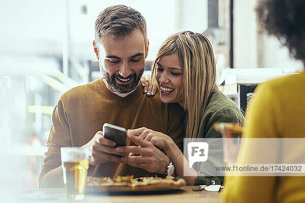 Happy male and female friends sharing smart phone in restaurant
