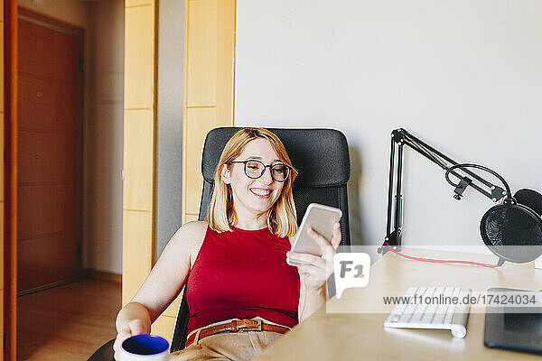 Smiling businesswoman using mobile phone while sitting on swivel chair at home office