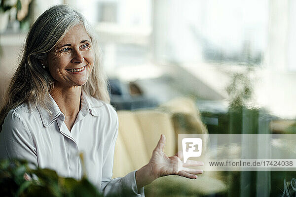 Smiling businesswoman with gray hair gesturing while sitting in cafe