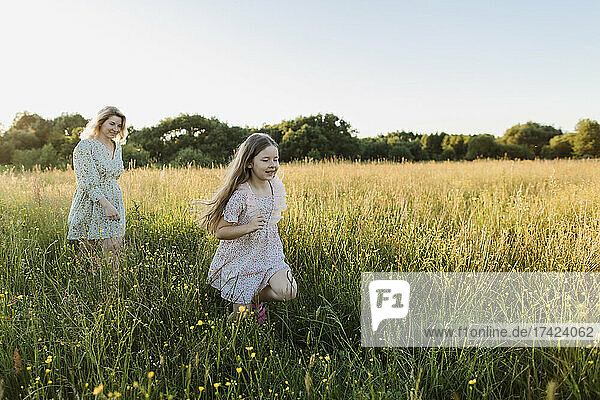 Playful girl and woman running at meadow during sunset