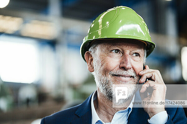 Lächelnder männlicher Manager  der in der Fabrik auf dem Smartphone spricht
