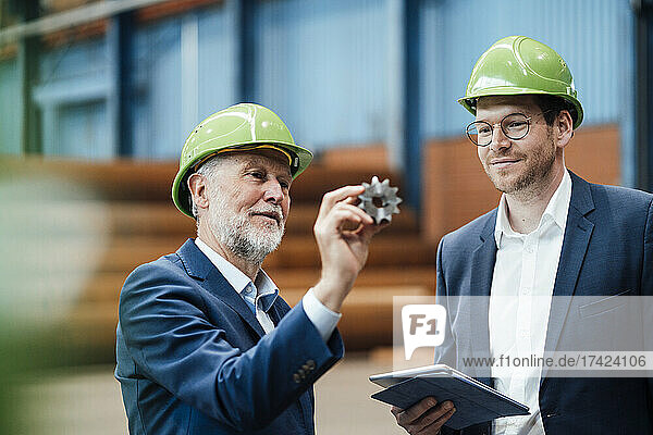 Male professional discussing over equipment with coworker in factory