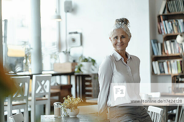 Smiling businesswoman leaning on table in cafe