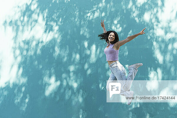 Carefree woman jumping by wall