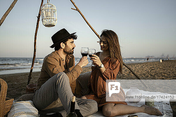 Couple toasting drink while sitting on picnic blanket