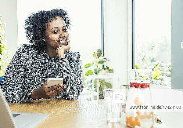Smiling businesswoman with mobile phone looking away at home office