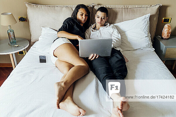 Junge queere Freundinnen benutzen Laptop  während sie zu Hause im Bett liegen