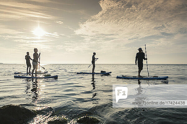Männer und Frauen  die bei Sonnenuntergang auf dem Meer paddeln lernen