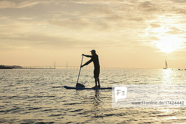 Seitenansicht eines Mannes  der bei Sonnenuntergang mit dem Paddelbrett ins Meer rudert