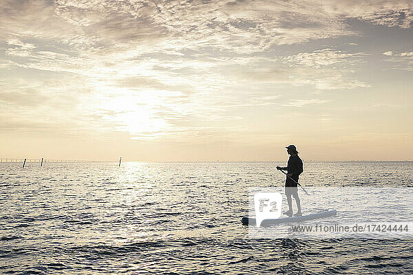 Mittlerer erwachsener Mann schaut weg  während er auf einem Paddleboard im Meer steht