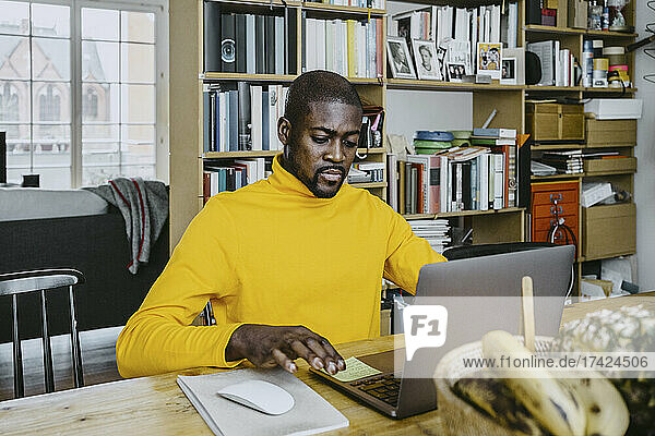 Männlicher Freiberufler  der einen Laptop benutzt  während er von zu Hause aus am Tisch arbeitet