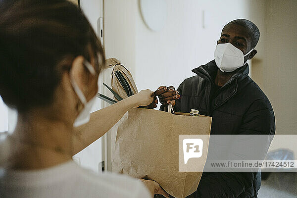 Mann liefert Lebensmittel an eine Frau  die während der Pandemie vor der Tür steht