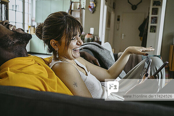 Glückliche Frau und Mann lachen  während sie mit Smartphones auf dem Sofa im Wohnzimmer zu Hause sitzen
