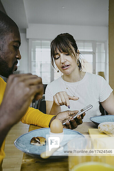 Woman discussing over smart phone with man while having breakfast at home