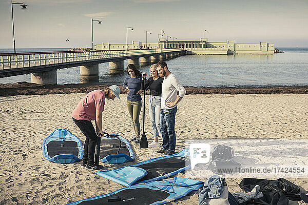 Männlicher Lehrer pumpt Paddleboard mit Freunden am Strand