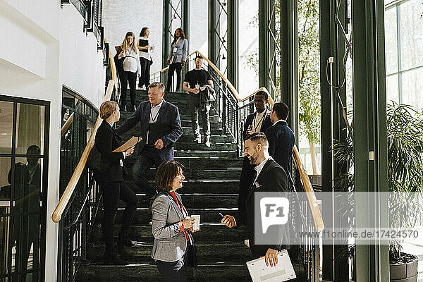 Männliche und weibliche Kollegen diskutieren zusammen  während sie bei einer Networking-Veranstaltung auf der Treppe stehen