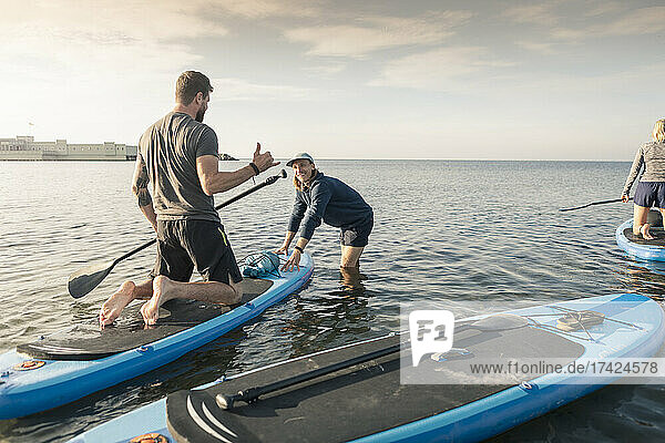 Mann lernt Paddelboard von männlichem Lehrer im Meer am Strand
