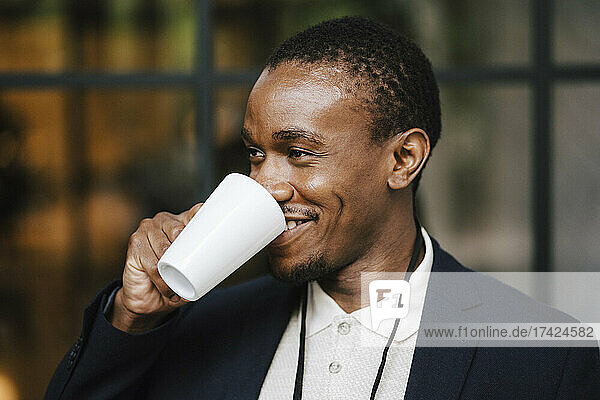 Lächelnder Geschäftsmann schaut weg  während er im Kongresszentrum Kaffee trinkt