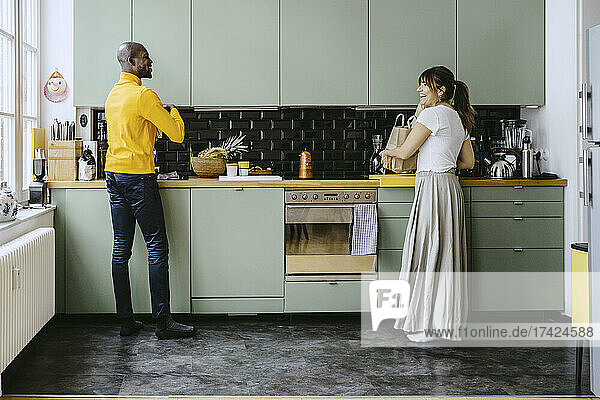 Lächelndes Paar in voller Länge  das sich bei der Hausarbeit in der Küche miteinander unterhält