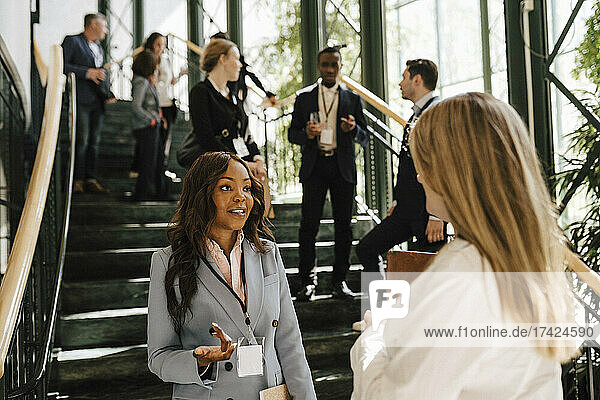 Geschäftsfrau gestikuliert  während sie mit einer weiblichen Fachkraft diskutiert  während sie an einer Treppe im Kongresszentrum steht